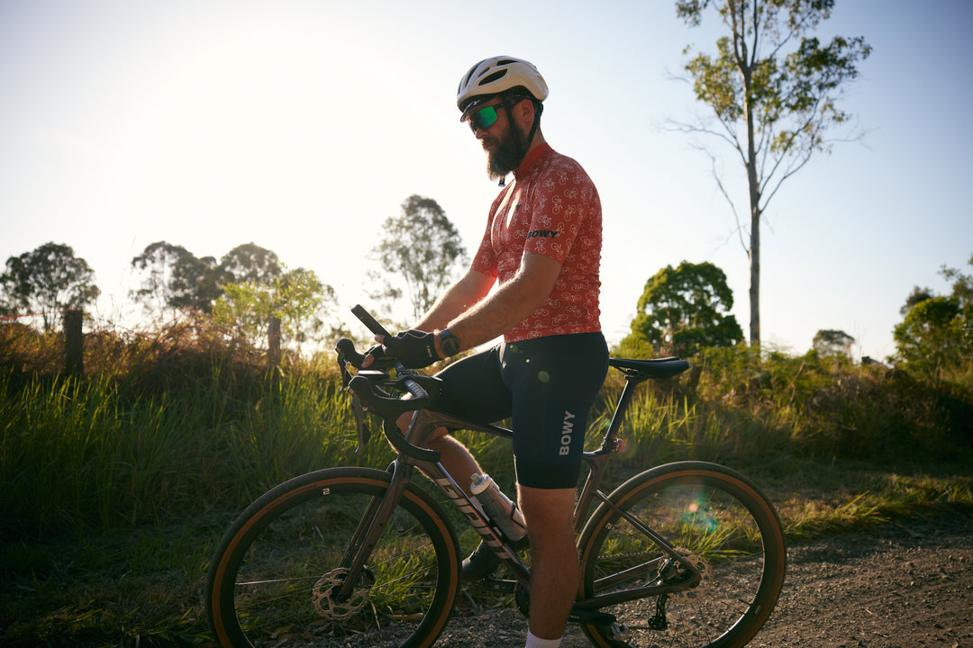 Allan standing on bike in burnt orange cycling jersey and cargo bib shorts