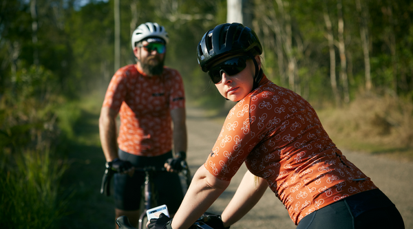 Female standing on bike in burnt orange cycling jersey - landscape